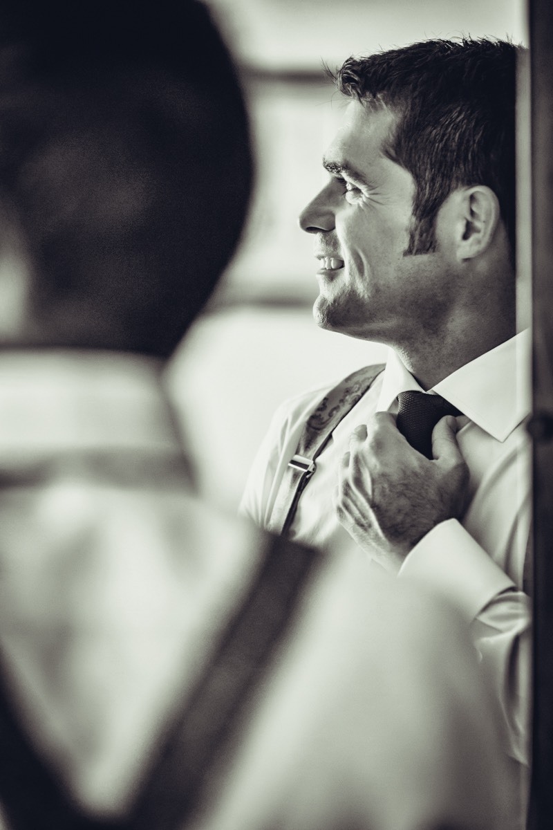 Novio vistiéndose reflejado en el espejo de un armario. Fotografía de boda realizada un en pueblo de cáceres