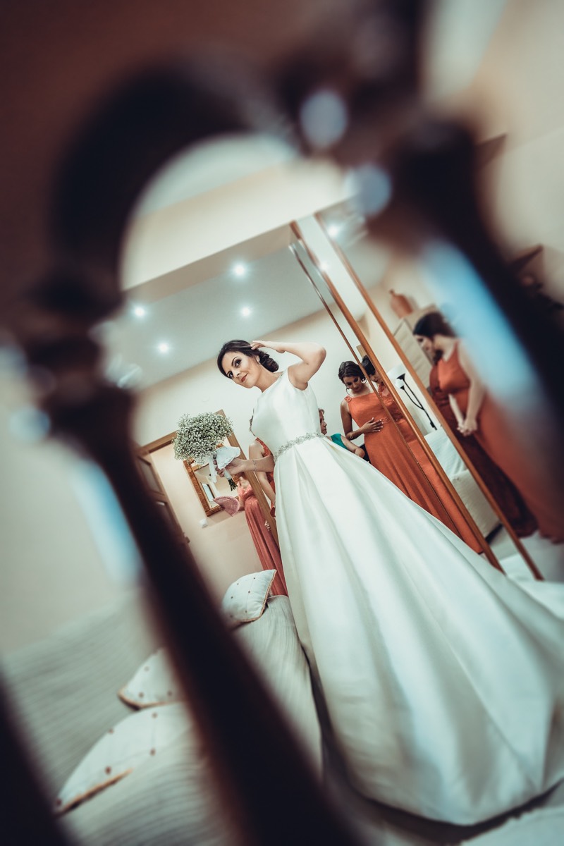 Encuadre original de una novia vista através de una silla mientras se toca el peinado