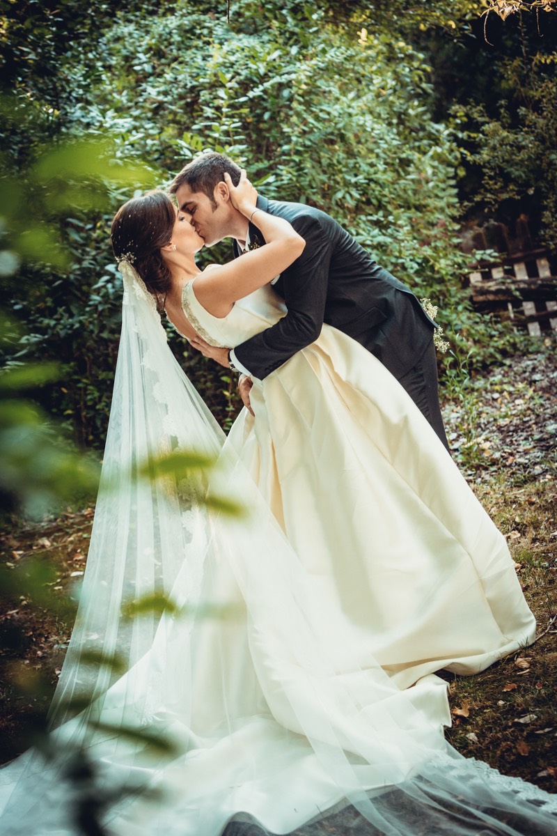 graciosa pose de una pareja de novios mientras se besan en un jardin durante su sesión de fotos de pareja en su boda