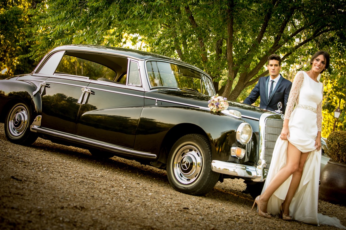 pareja de novios recién casados posando delante del coche de boda, un mercedes de época. Reportaje fotográfico de boda realizado por Uli para Bodas con fotos, fotógrafos de boda en Madid. España